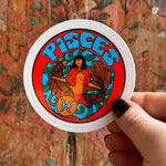 Someone holding the Pisces Zodiac 3 Inch Sticker in front of a wooden background.