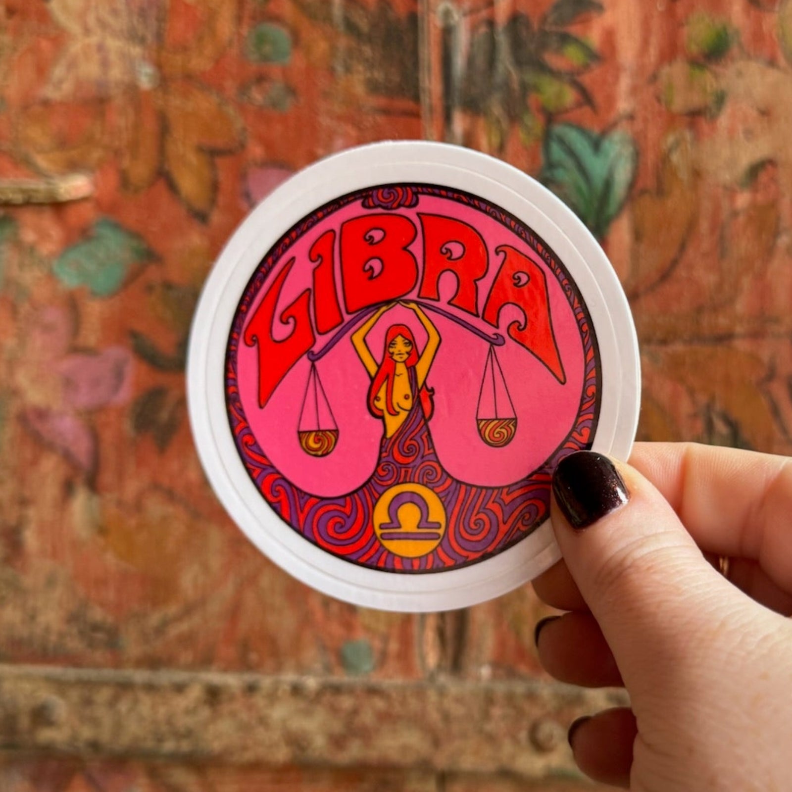 Someone holding the Libra Zodiac 3 Inch Sticker in front of a wooden background.