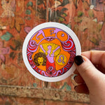 Someone holding the Leo Zodiac 3 Inch Sticker in front of a wooden background.