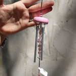 Someone holding the Rose Gem Drop Wind Chime in front of a white cement wall.