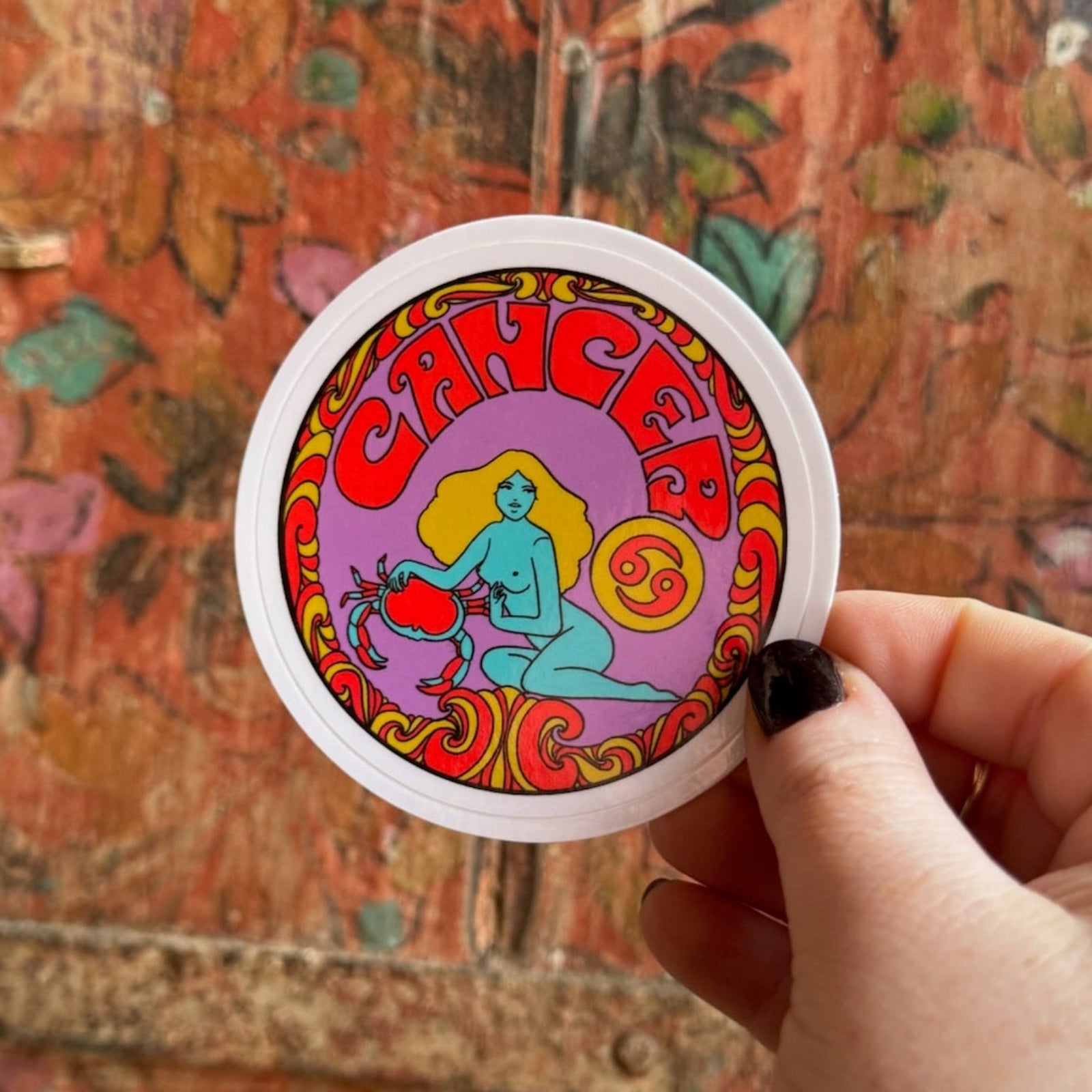 Someone holding the Cancer Zodiac 3 Inch Sticker in front of a wooden background.
