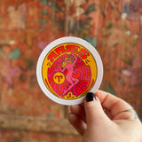Someone holding the Aries Zodiac 3 Inch Sticker in front of a wooden background.