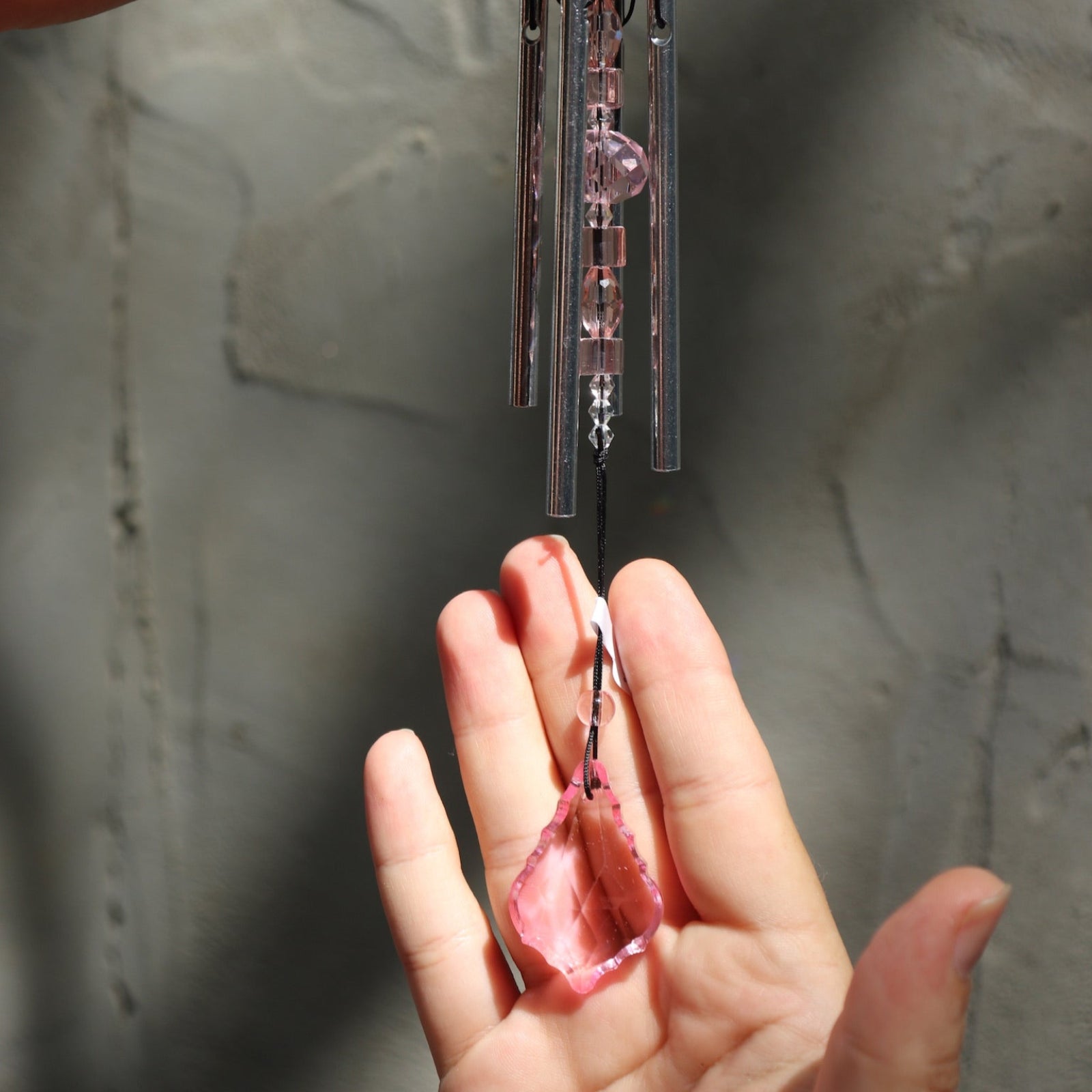 Someone holding the Rose Gem Drop Wind Chime in front of a white cement wall.