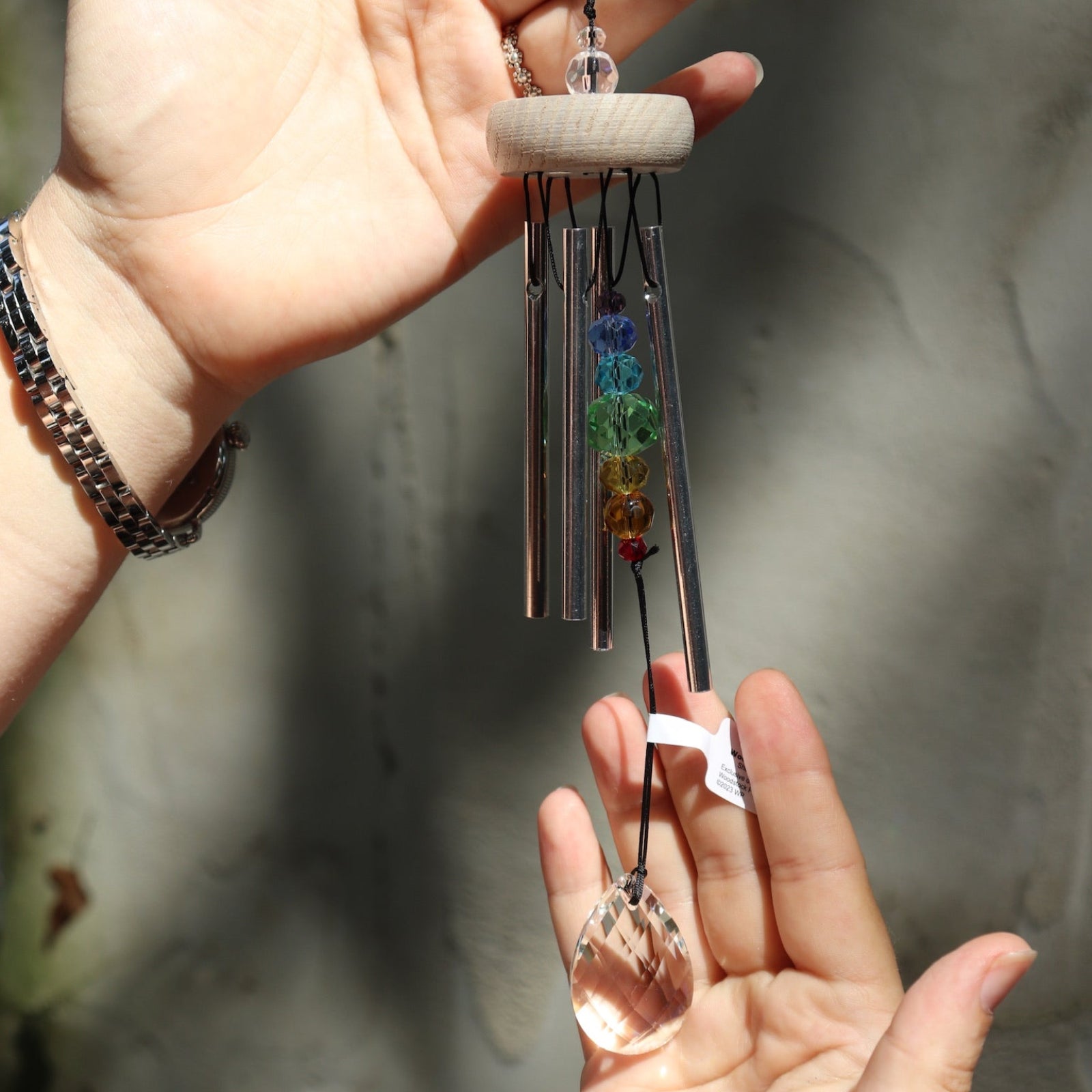 Someone holding the Prism Gem Drop Wind Chime in front of a white cement wall.