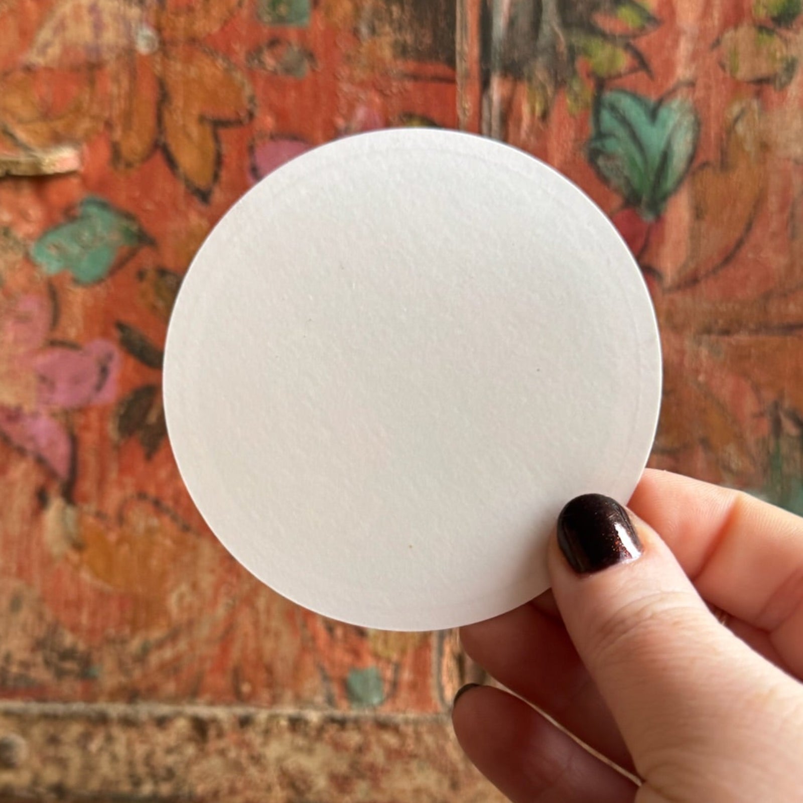 Someone holding the Zodiac 3 Inch Sticker in front of a wooden background, showing off the back.