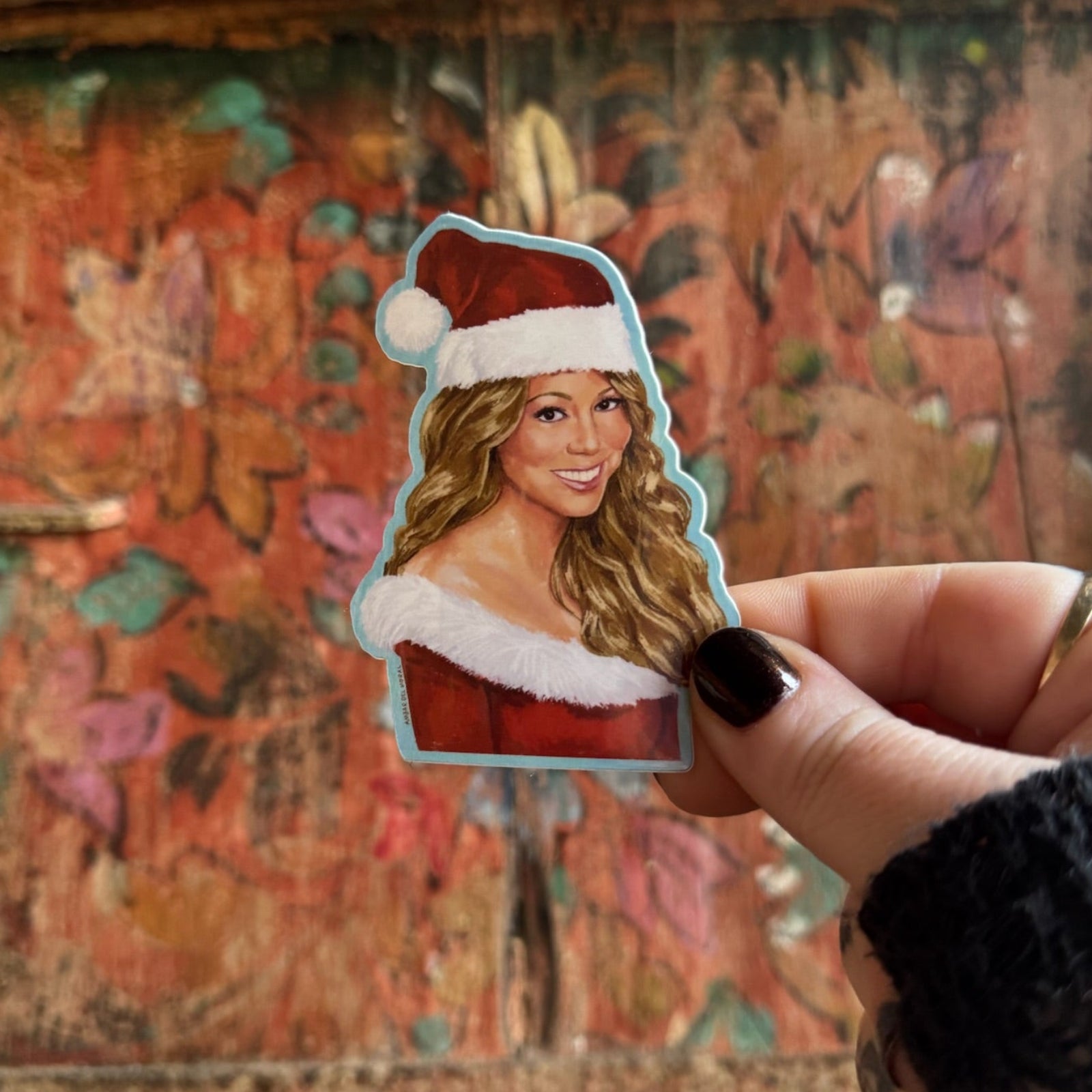 Someone holding the Mariah Carey Christmas Sticker in front of a wooden background.