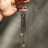 Someone holding the Prism Gem Drop Wind Chime in front of a white cement wall.