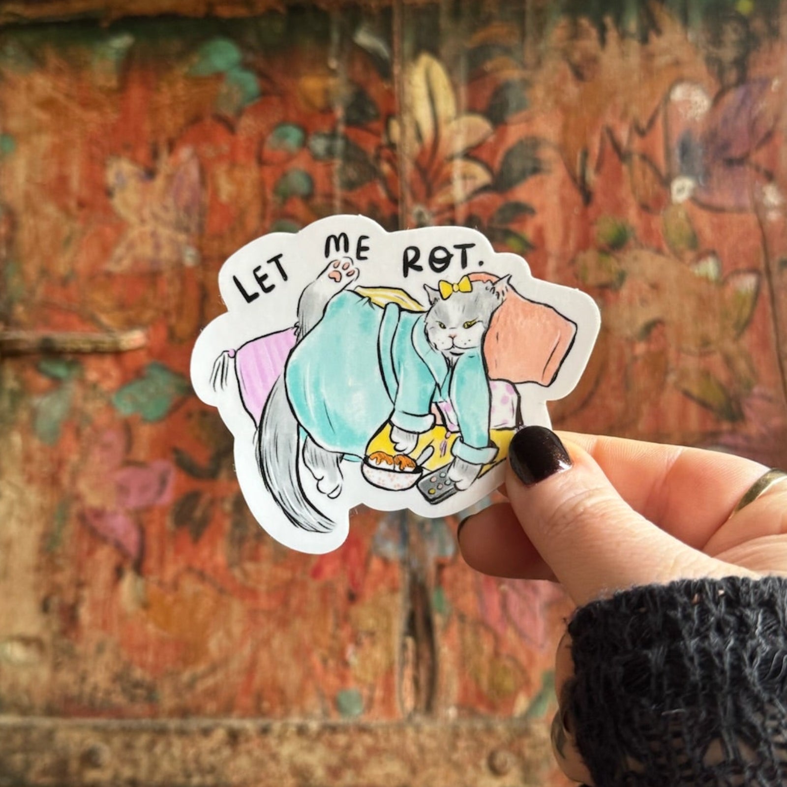 Someone holding the Couch Cat Vinyl Sticker in front of a wooden background.