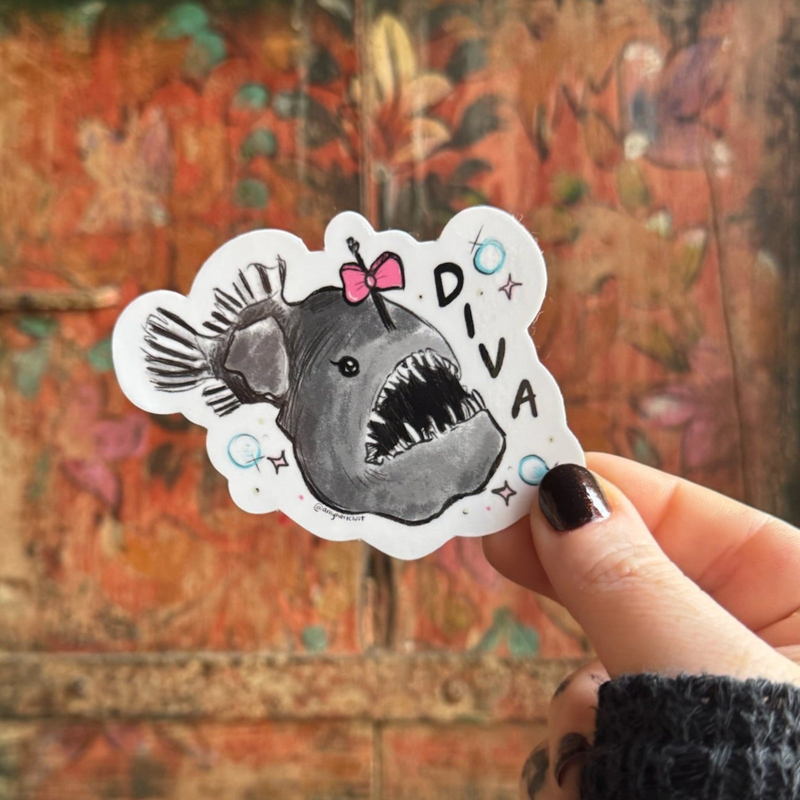 Someone holding the Anglerfish Diva Vinyl Sticker in front of a wooden background.
