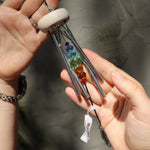 Someone holding the Prism Gem Drop Wind Chime in front of a white cement wall.