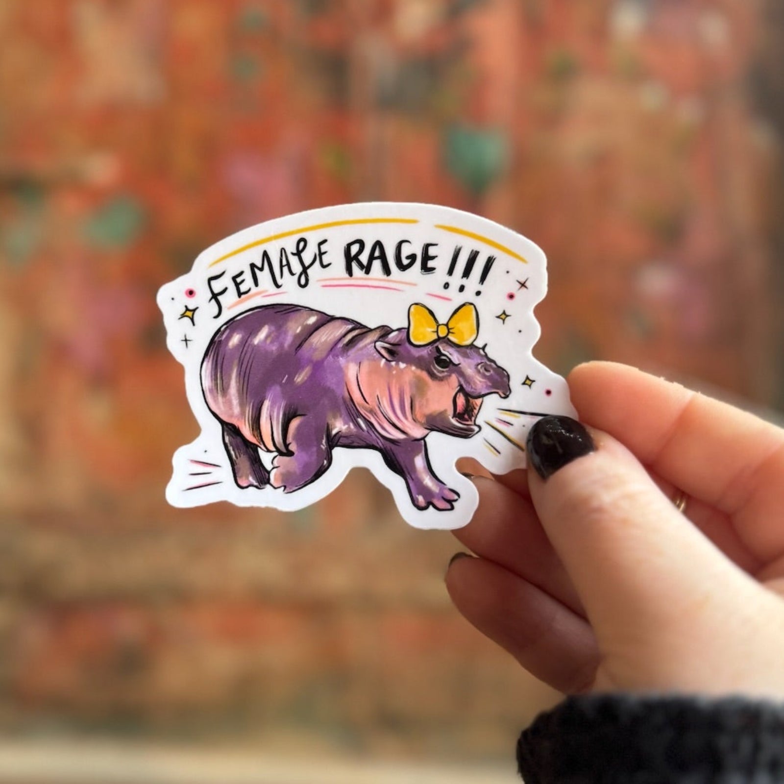 Someone holding the MooDeng Female Rage Vinyl Sticker in front of a wooden background.