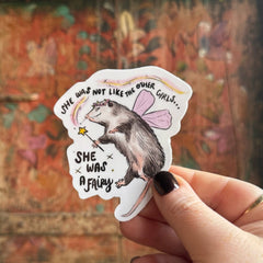 Someone holding the Fairy Possum Vinyl Sticker in front of a wooden background.