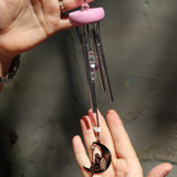 An up-close image of someone holding the Fairy Fantasy Woodstock Wind Chime in front of a white cement wall.
