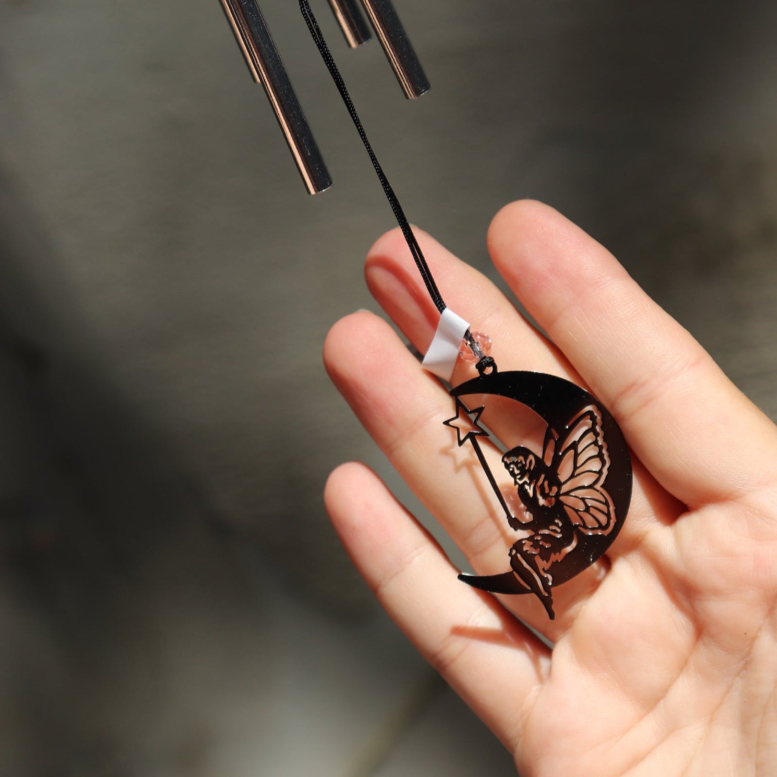 An up-close image of someone holding the Fairy Fantasy Woodstock Wind Chime in front of a white cement wall.