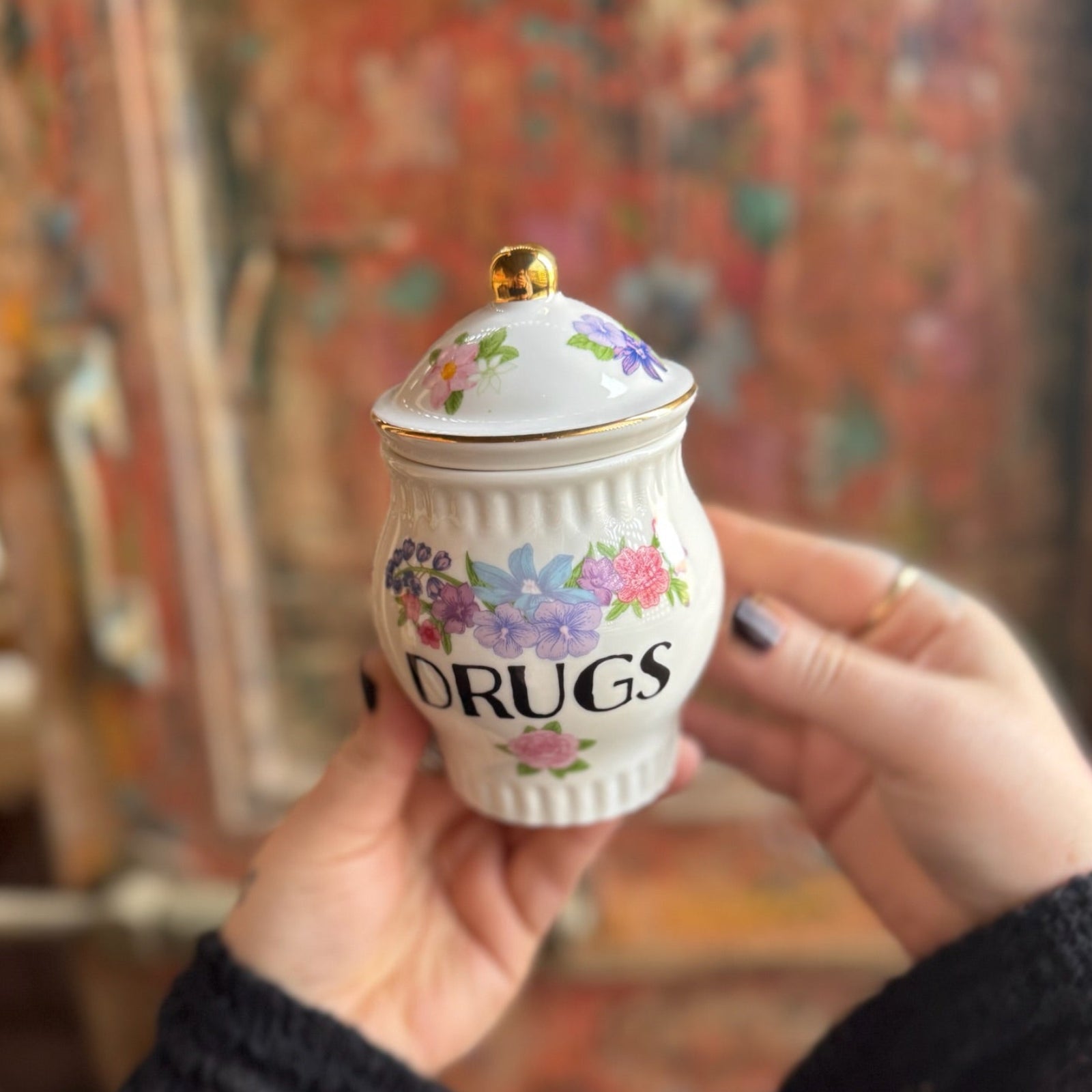 Someone holding the Grandma's Floral Ceramic Stash Jar in front of a wooden background.