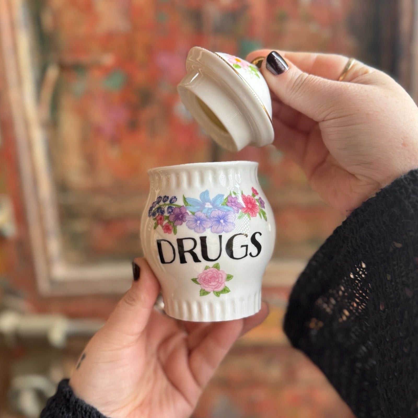 Someone holding the Grandma's Floral Ceramic Stash Jar in front of a wooden background, with the lid off.