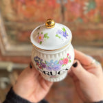 Someone holding the Grandma's Floral Ceramic Stash Jar in front of a wooden background, showing the top.