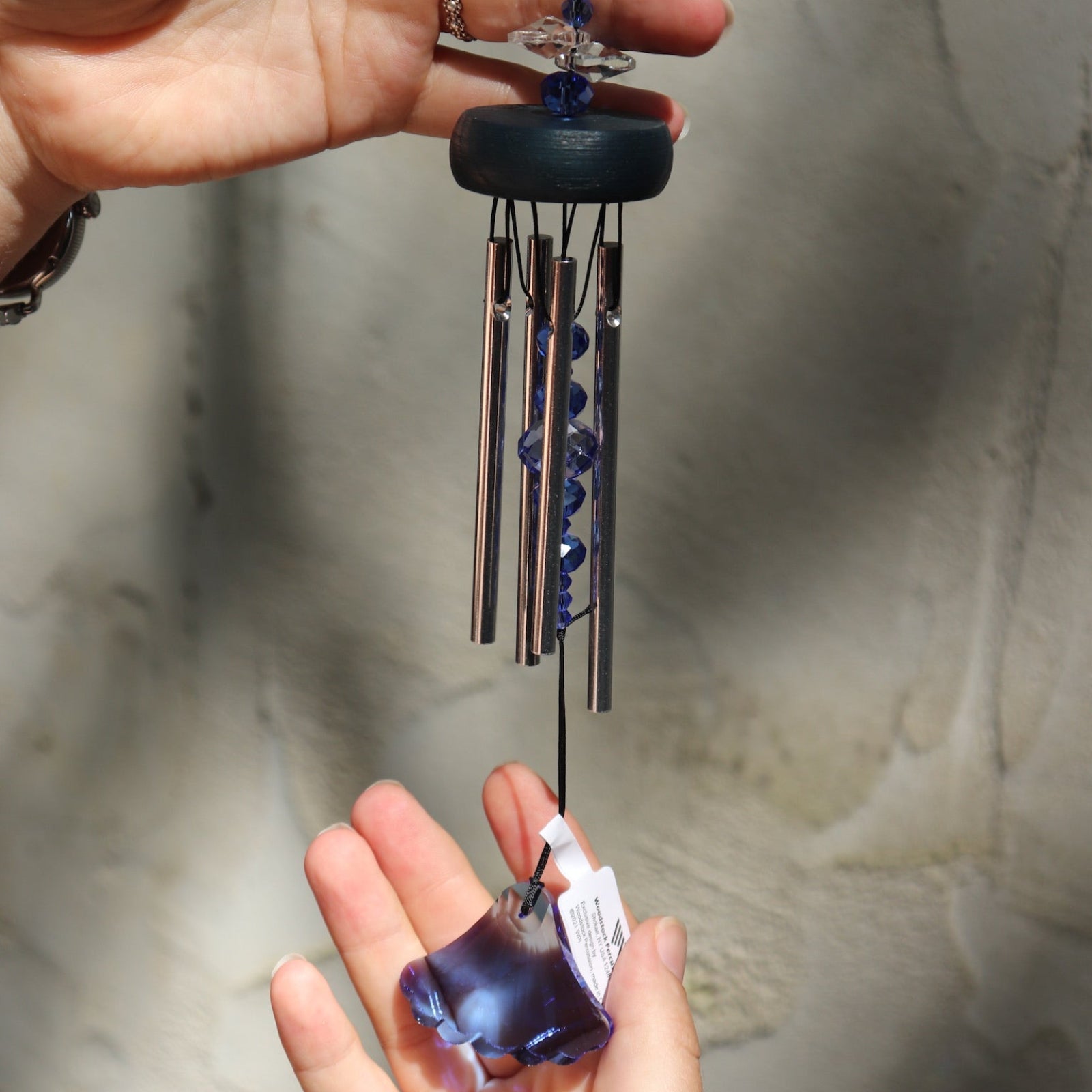 Someone holding the Sapphire Gem Drop Wind Chime in front of a white cement wall.