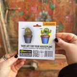 Someone holding the Wind Dancers Fancy Plants Diorama Kit  in front of a wooden background, showing off the back.