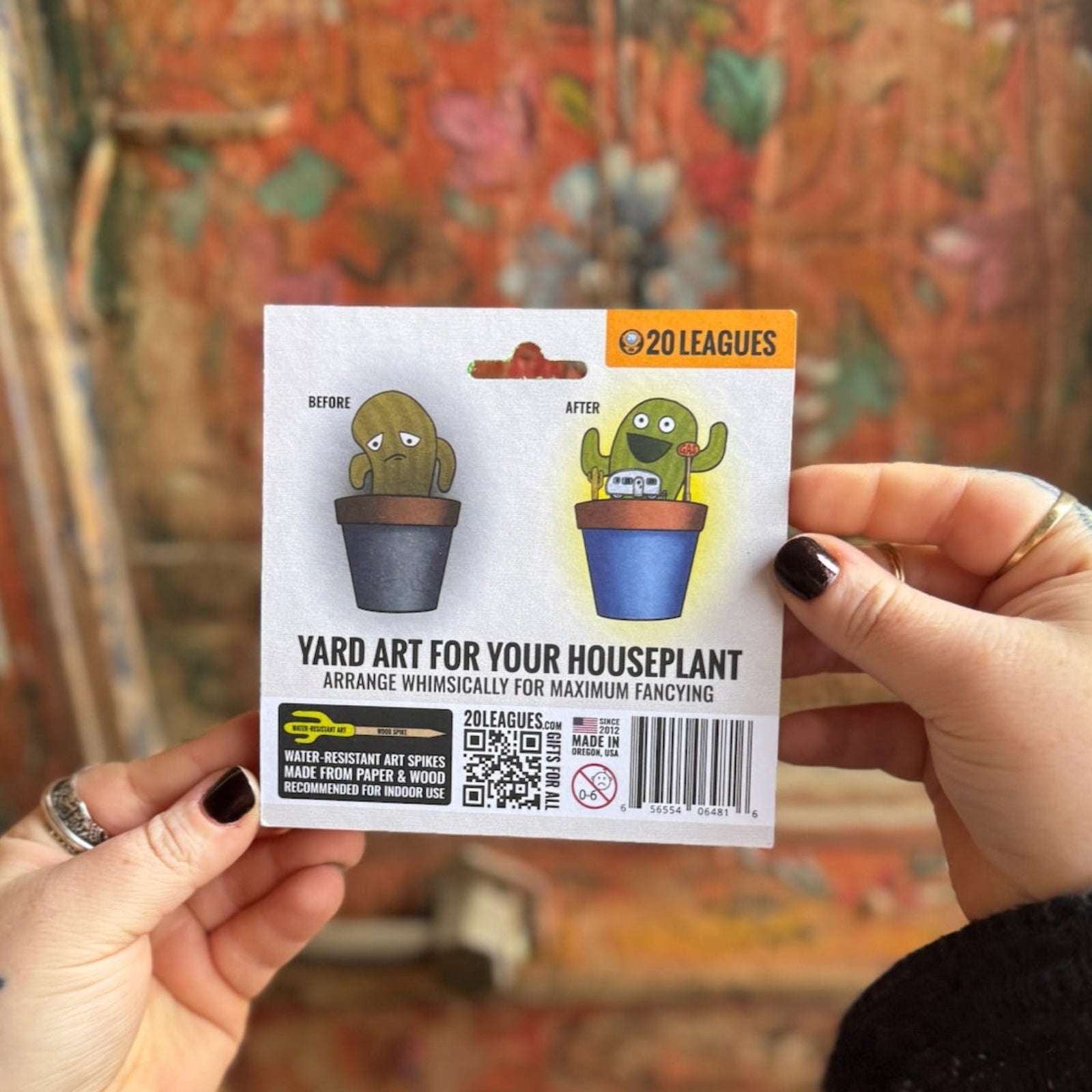 Someone holding the Wind Dancers Fancy Plants Diorama Kit  in front of a wooden background, showing off the back.