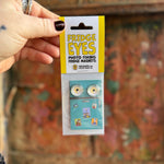 Someone holding the Fridge Eyes Magnets in front of a wooden background.