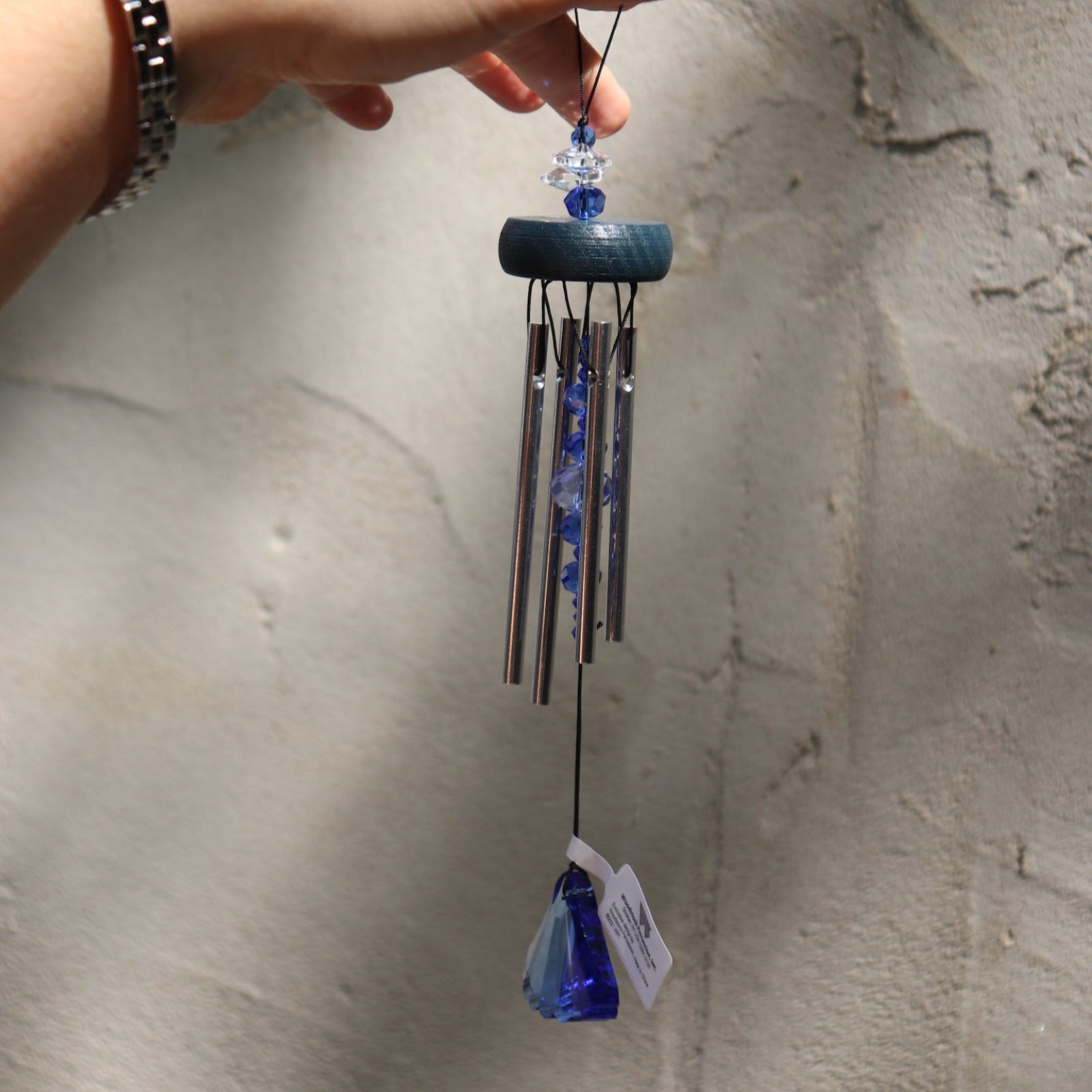Someone holding the Sapphire Gem Drop Wind Chime in front of a white cement wall.