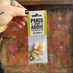 Someone holding the Pugs from Above Parachute Toy in front of a wooden background.