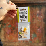 Someone holding the Pugs from Above Parachute Toy in front of a wooden background.