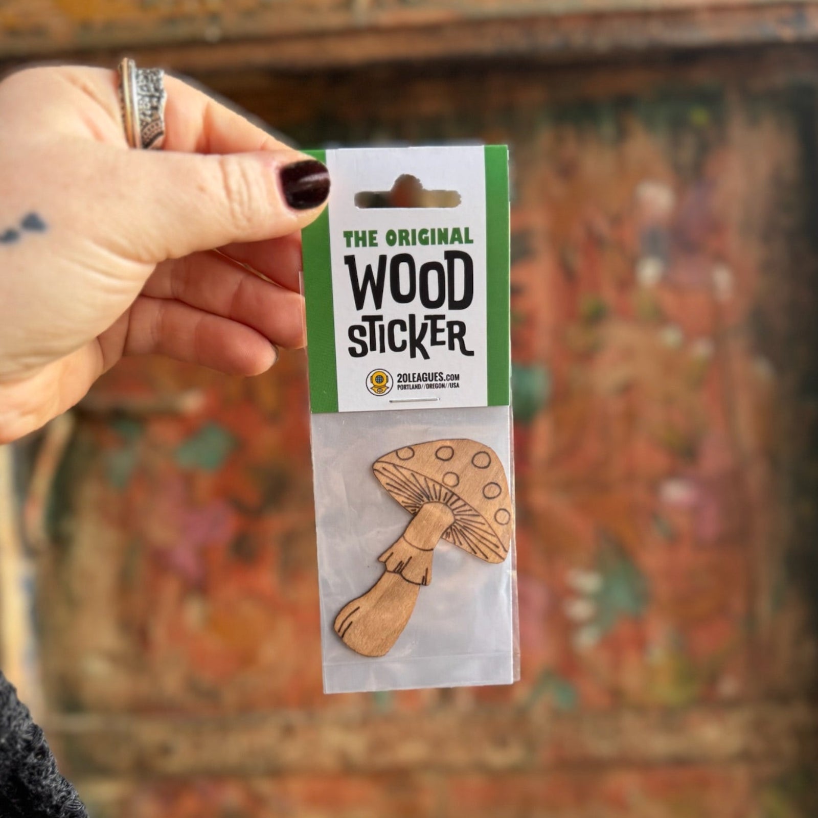 Someone holding the Mushroom Wood Sticker in front of a wooden background.