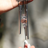 An up-close image of the faux crystals in the Rose Quartz Heart Wind Chime in front of a white cement wall.