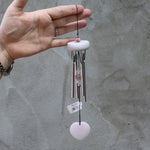 Someone holding the Rose Quartz Heart Wind Chime in front of a white cement wall.