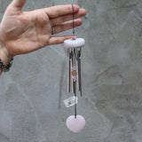 Someone holding the Rose Quartz Heart Wind Chime in front of a white cement wall.