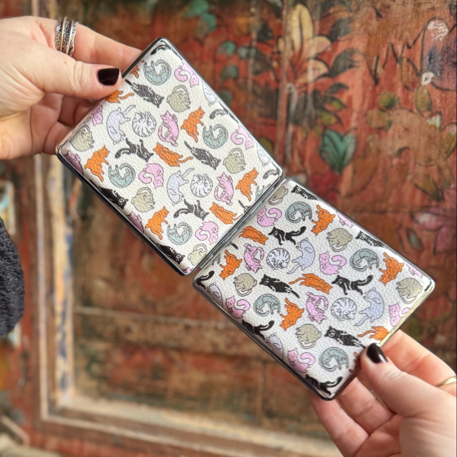 Someone holding the Cozy Cat Hardcover Cigarette Case in front of a wooden background, showing off the back.