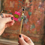 Someone holding the Stone Wand Cigarette Metal Holder & Packing Tool in front of a wooden background.