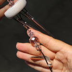 An up-close image of the faux crystals in the Rose Quartz Heart Wind Chime in front of a white cement wall.