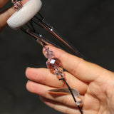 An up-close image of the faux crystals in the Rose Quartz Heart Wind Chime in front of a white cement wall.