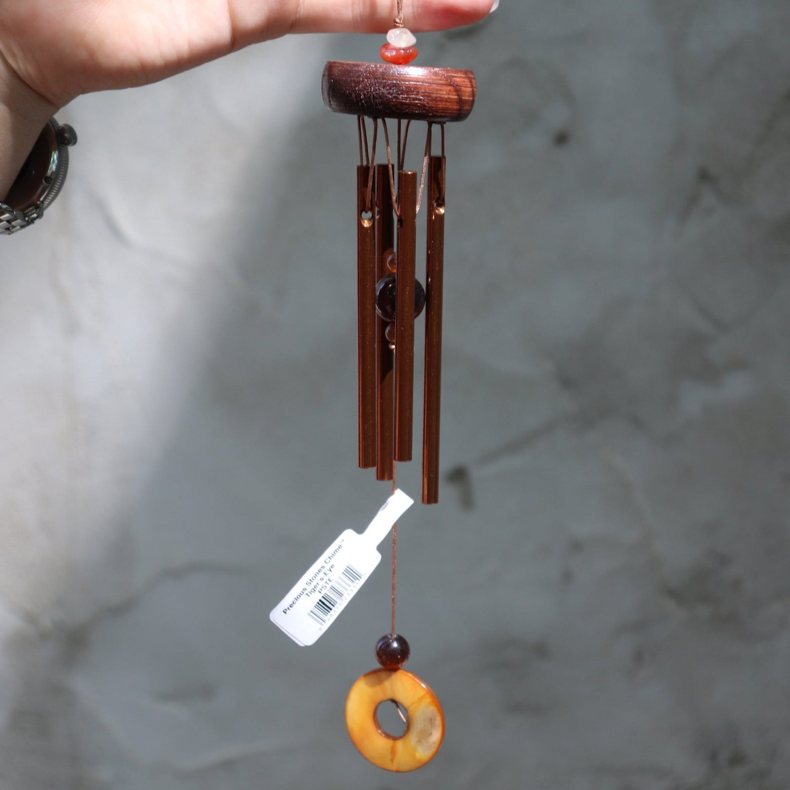 Someone holding the Tiger's Eye Precious Stones Wind Chime in front of a white wall.