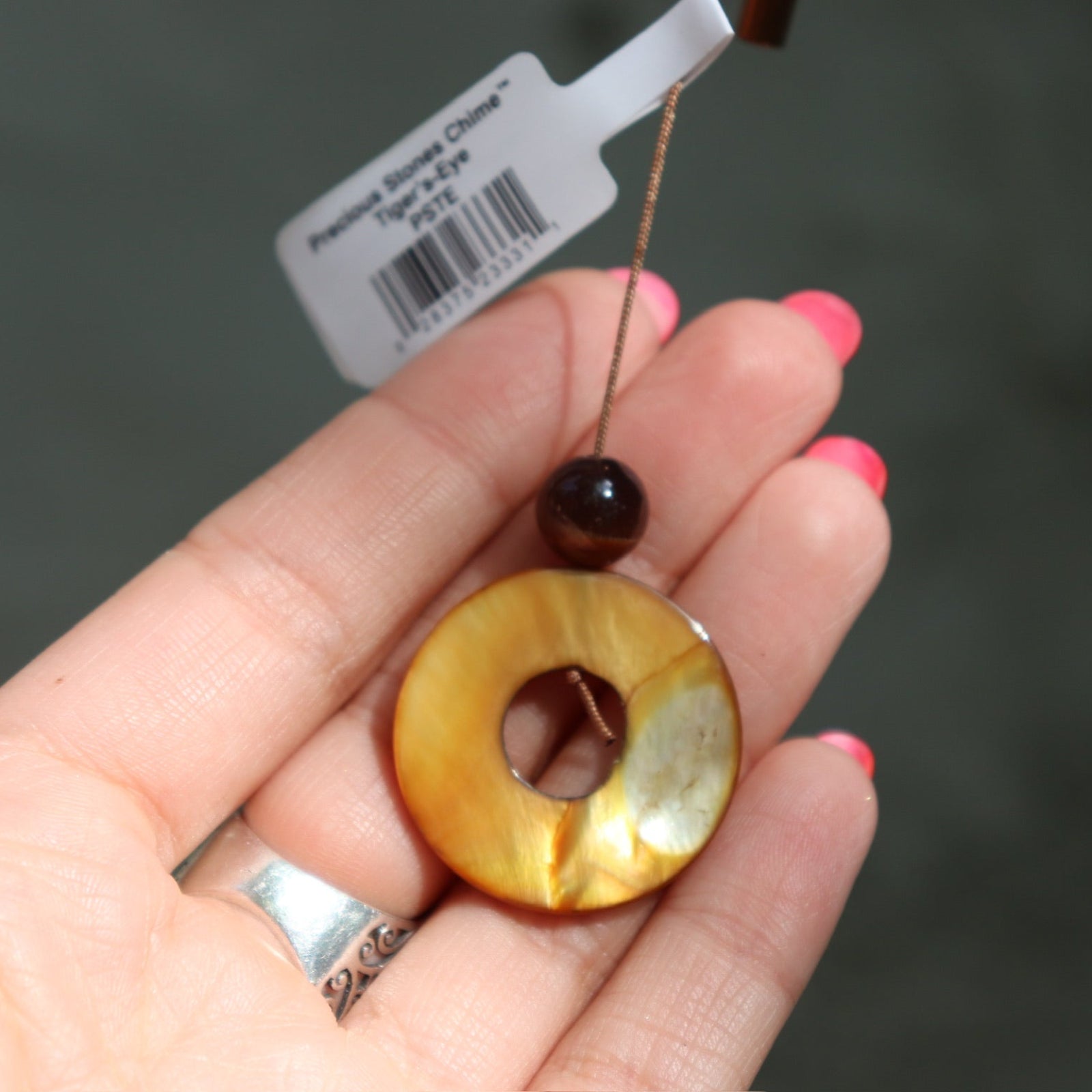 An up-close image of someone holding the ring accent from the Tiger's Eye Precious Stones Wind Chime in front of a white wall.