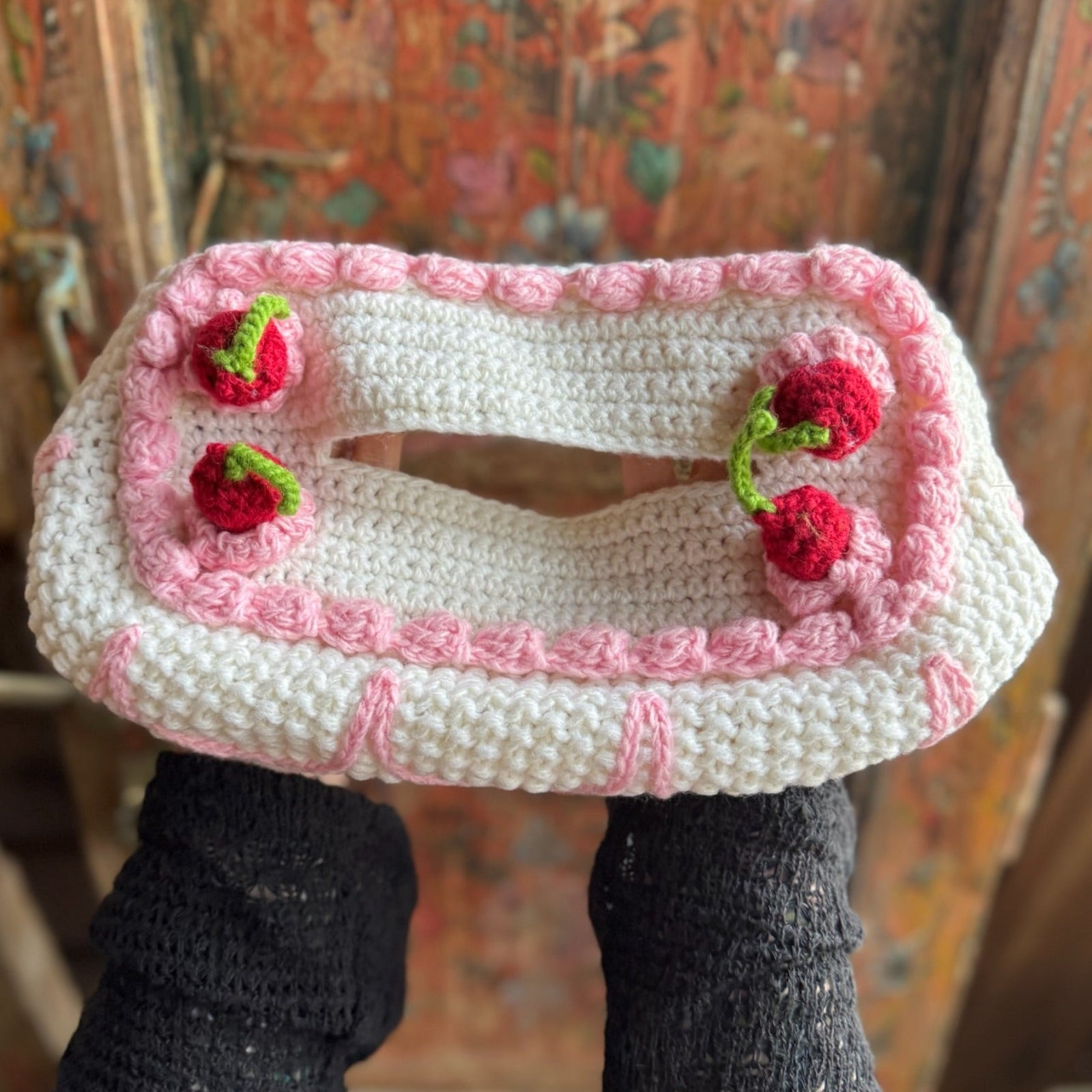 Someone holding the Crochet Coquette Cake Tissue Box Cover in front of a wooden background.