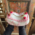 Someone holding the Crochet Coquette Cake Tissue Box Cover in front of a wooden background.