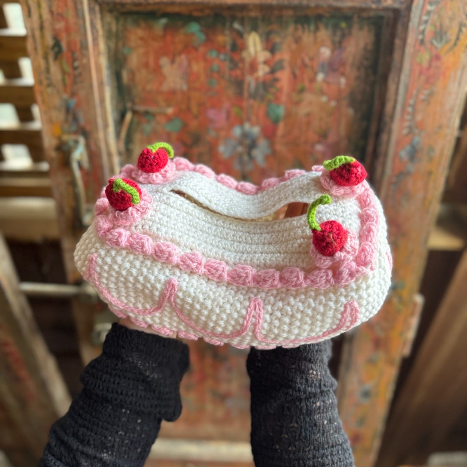 Someone holding the Crochet Coquette Cake Tissue Box Cover in front of a wooden background.