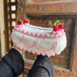 Someone holding the Crochet Coquette Cake Tissue Box Cover in front of a wooden background.