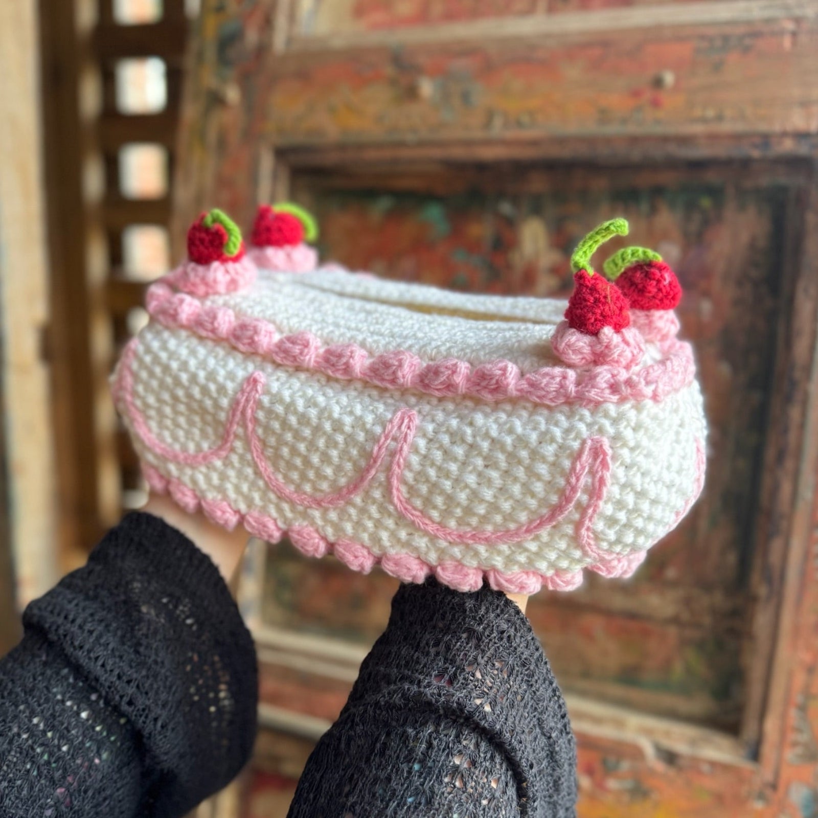 Someone holding the Crochet Coquette Cake Tissue Box Cover in front of a wooden background.