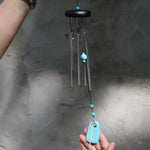 Someone holding the Turquoise Woodstock Chakra Wind Chime in front of a white wall.