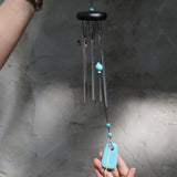 Someone holding the Turquoise Woodstock Chakra Wind Chime in front of a white wall.