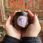 Someone holding the Herbal Renewal Soy Wax 3 oz Candle in front of a wooden background.