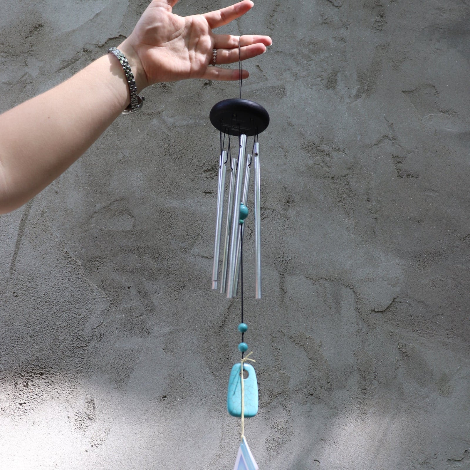 Someone holding the Turquoise Woodstock Chakra Wind Chime in front of a white wall.