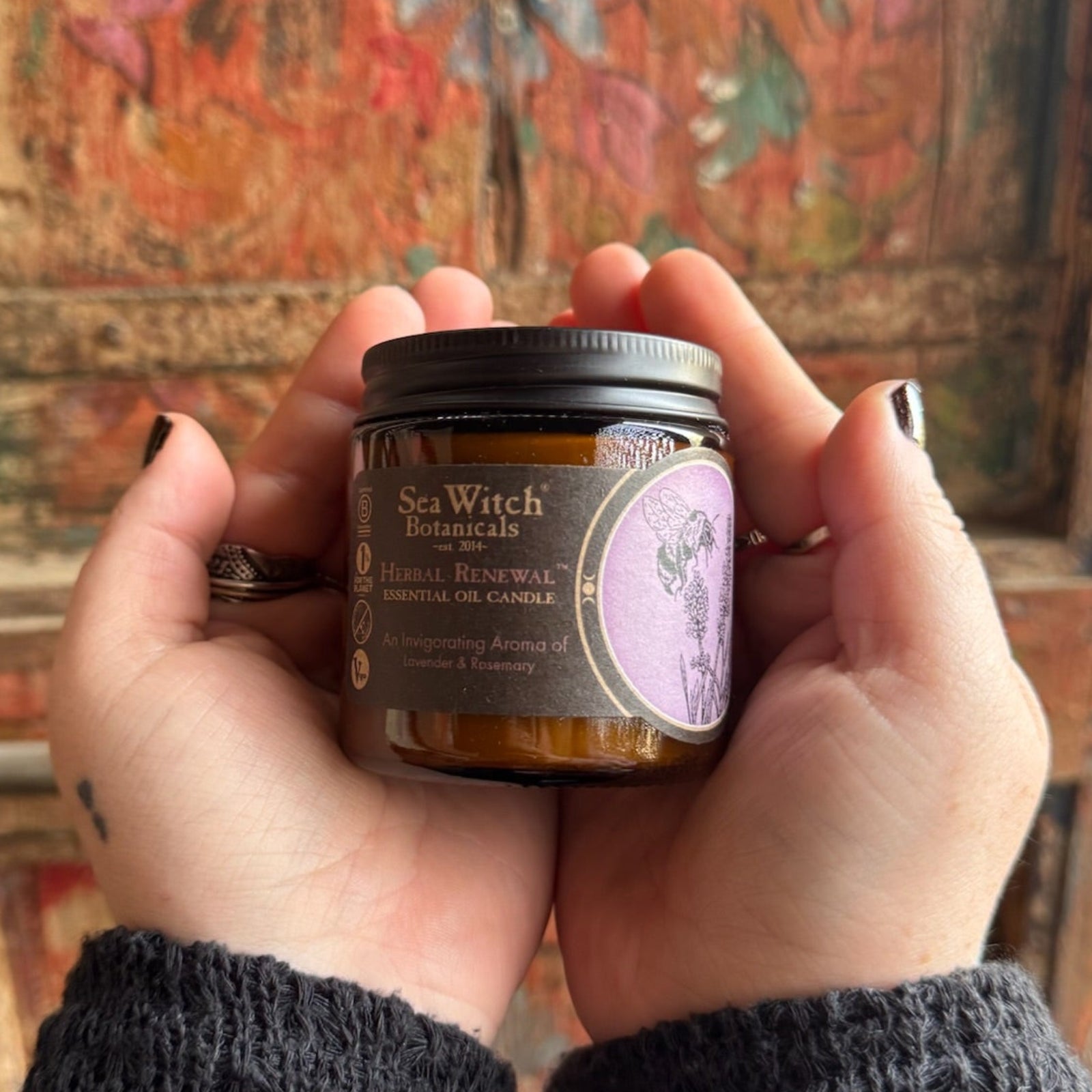 Someone holding the Herbal Renewal Soy Wax 3 oz Candle in front of a wooden background.