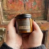 Someone holding the Herbal Renewal Soy Wax 3 oz Candle in front of a wooden background.