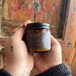 Someone holding the White Lodge Soy Wax 3 oz Candle in front of a wooden background.